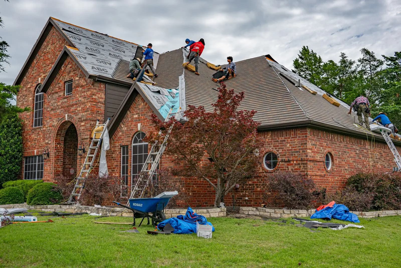 Roofing crew working on a brick house with tarps protecting the yard