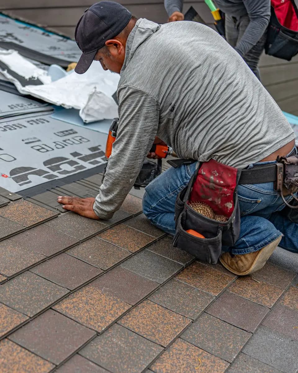 Roofer in a tool belt nailing new shingles on a residential roof