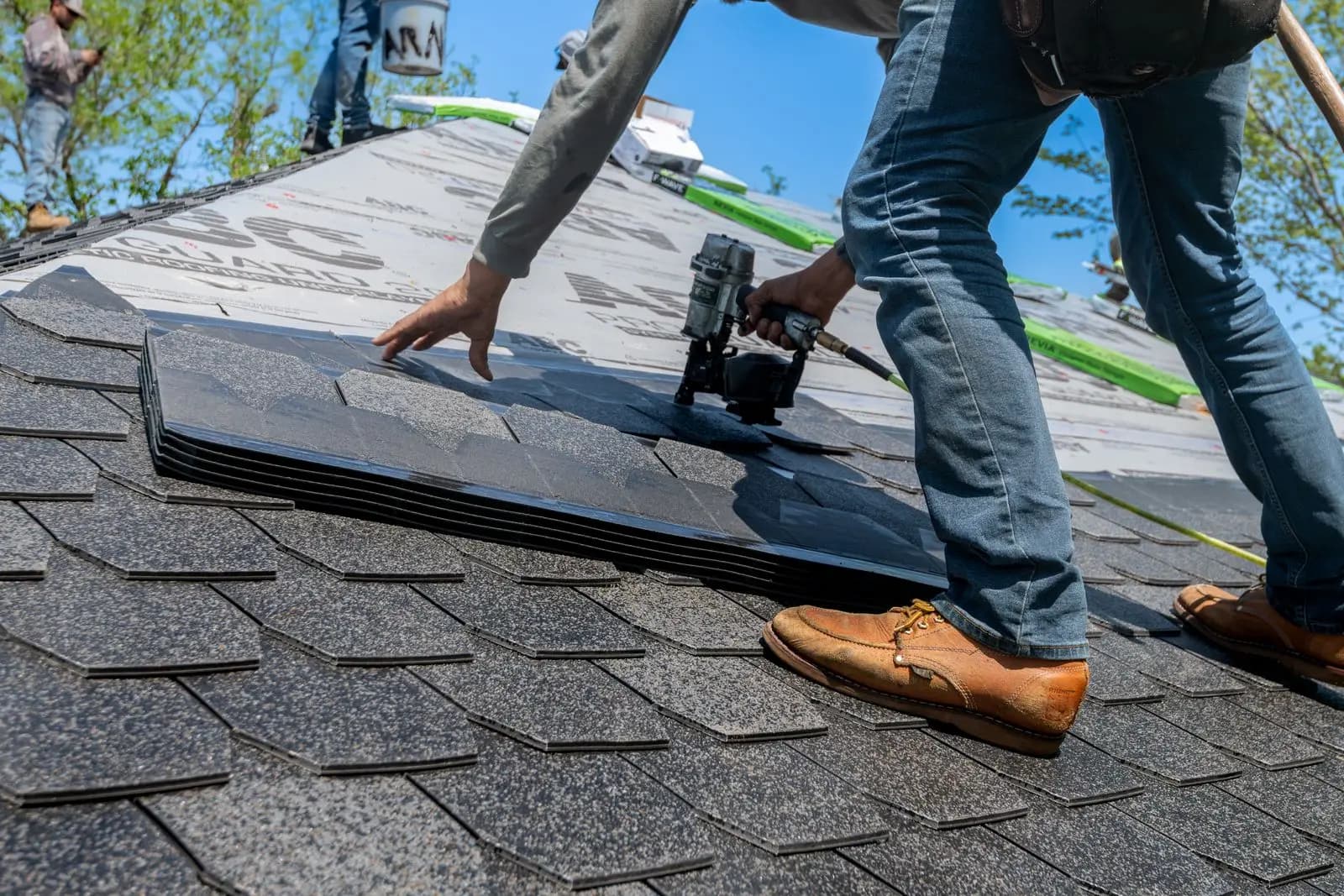 Roofer nailing asphalt shingles with a nail gun